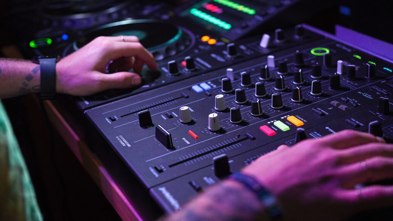 Close-up of hands working a DJ mixer under neon rim light